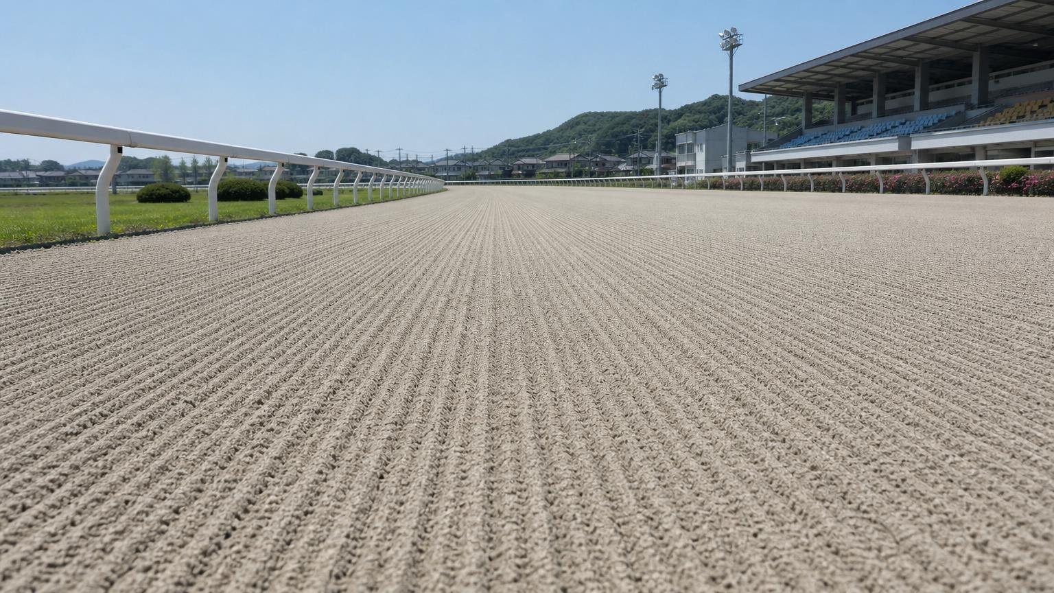 園田競馬場をイメージした砂のコース。レース前のハロー掛けを終えた無人の走路が、走行方向に走る細い筋を残して奥へ続いている