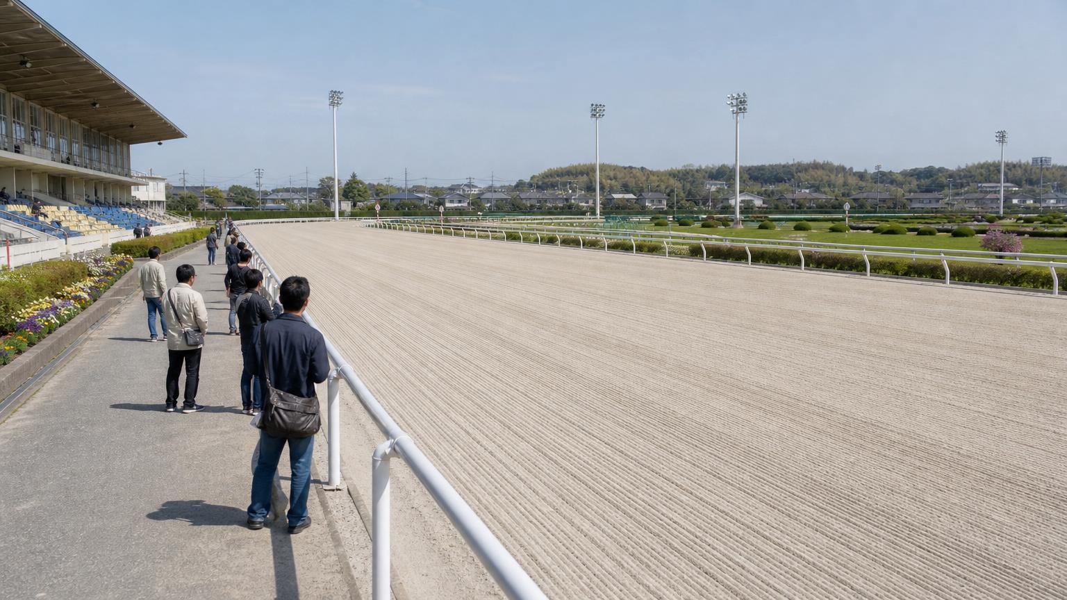 盛岡競馬場をイメージした地方競馬場の全景。手前にスタンドと立ち見の広場、その先の外ラチの向こうに砂のコースが広がっている