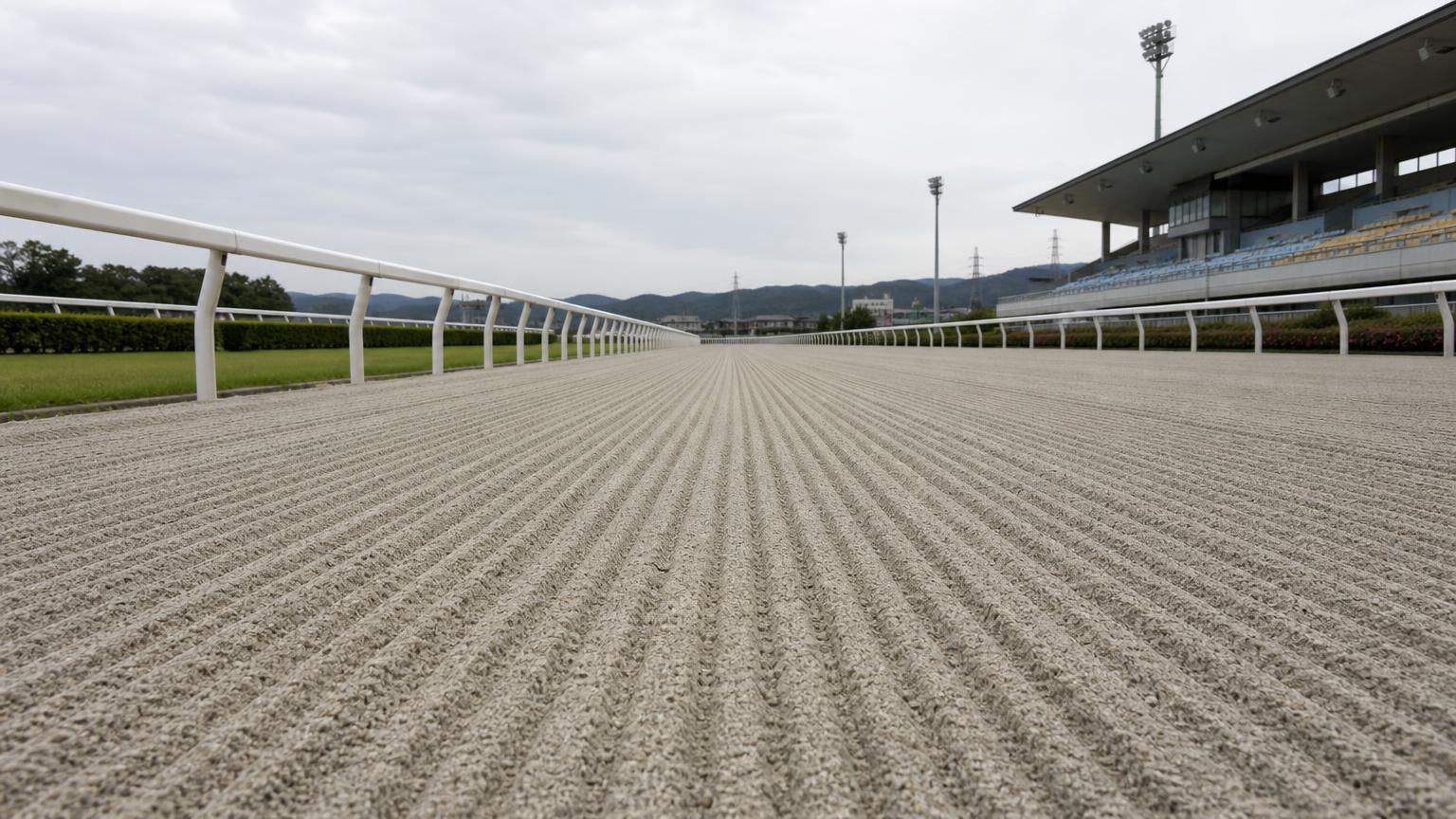 名古屋（弥富）競馬場をイメージした砂のコース。レース前のハロー掛けを終えた無人の走路が、走行方向に走る細い筋を残して奥へ続いている